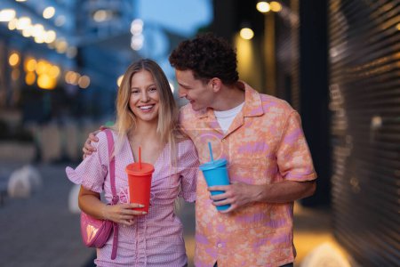 Photo for Gen Z couple in pink outfits leaving the cinema with drinks in hand. The young zoomers watched a movie addressing the topic of women, her position in the world, and body image. - Royalty Free Image