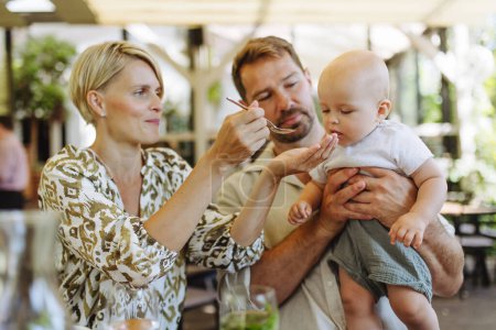 Téléchargez les photos : Parents dans un restaurant nourrissant un petit bébé. Dîner en famille dans un restaurant. - en image libre de droit
