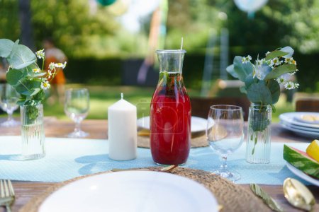 Foto de Primer plano de una mesa fija en una fiesta de verano en el jardín. Mesa con copas, limonada de frutas, fruta fresca y ensalada y delicada decoración floral. - Imagen libre de derechos