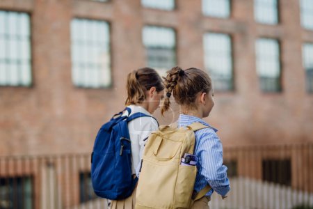 Foto de Vista trasera de dos colegialas que van a la escuela. Compañeros de clase con mochilas frente al edificio de la escuela. - Imagen libre de derechos