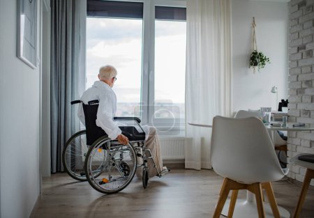 Téléchargez les photos : Un aîné en fauteuil roulant passe du temps seul dans son appartement. Concept de solitude et de dépendance des retraités. - en image libre de droit