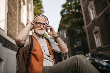 Téléchargez les photos : Gros plan d'un aîné dans la rue. Homme cool âgé écoutant de la musique à l'extérieur, s'amusant. Concept de vieil homme jeune de cœur. - en image libre de droit