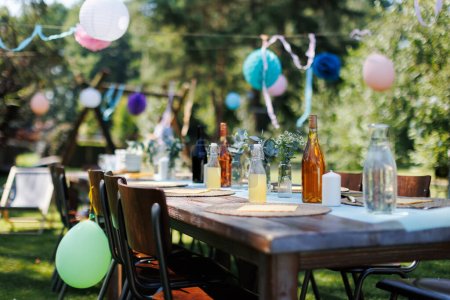 Photo for Close up shot of a set table at a summer garden party. Table setting with glasses, fruit lemonade, fresh fruits and salads and delicate floral decoration. Colorful paper decorations for party. - Royalty Free Image
