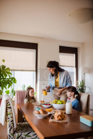 Téléchargez les photos : Mère prépare le petit déjeuner et verse du jus pour les enfants, le matin. Amour maternel et soins pour le ménage et la famille. - en image libre de droit