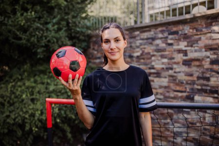 Photo for Beautiful female football player standing by the football goal with a ball in her hand. The woman plays soccer for relaxation. Concept of mental health and sport. - Royalty Free Image