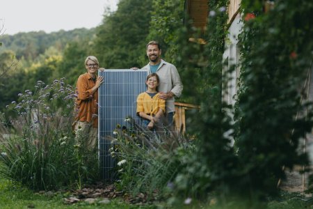 Father mother and daughter standing in garden holding solar panel. Solar energy and sustainable lifestyle of young family. Concept of green energy and sustainable future for next generations.