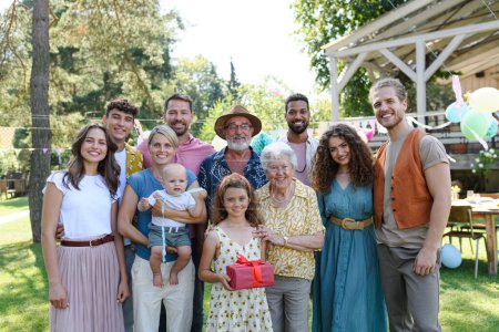 Family portrait at an outdoor summer garden party. Family and friends standing and posing for a group photo. Multigenerational family.