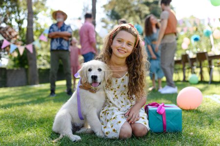 Foto de Fiesta de cumpleaños en el jardín para niña. Hermosa cumpleañera recibió un cachorro como regalo de cumpleaños. - Imagen libre de derechos