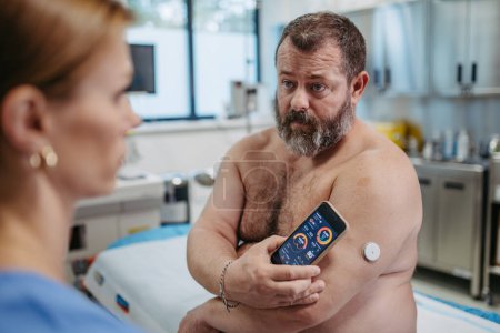 Téléchargez les photos : Médecin connectant les patients moniteur de glucose continu avec smartphone, pour vérifier son taux de sucre dans le sang en temps réel. Obèse, l'homme en surpoids est à risque de développer le diabète de type 2. Concept de santé - en image libre de droit