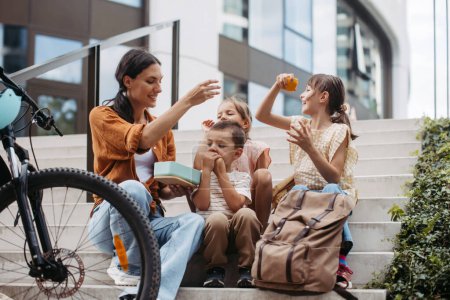 Photo for Children and mother have a healthy snack in the city after school. The family sitting on concrete steps in the city, resting and eating home made snack, fruit. - Royalty Free Image