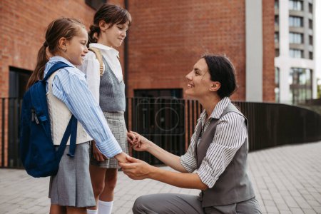 Photo for A hard-working, ambitious mother preparing her daughters for school, saying goodbye to them in front of the school building, and heads to work. Concept of work-life balance for women. - Royalty Free Image