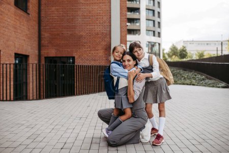 Photo for Working mother picking up daughters from school, greeting them in front of the school building, and heads to work. Concept of work-life balance for women. - Royalty Free Image