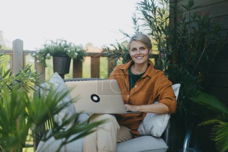 Photo for Woman working in garden, with laptop on legs. Businesswoman working remotely from outdoor homeoffice, thinking about new business or creative idea. Concept of outdoor home office. - Royalty Free Image