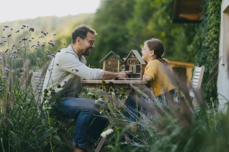 Téléchargez les photos : Père avec sa fille faire un hôtel insecte, ou une maison d'insectes à l'extérieur dans le jardin. Fille en apprendre davantage sur les insectes, l'écosystème du jardin et la biodiversité. - en image libre de droit