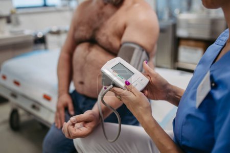 Foto de Médico midiendo la presión arterial, examinando la hipertensión, usando monitor de presión arterial. Obesidad que afecta la salud de los hombres de mediana edad. Concepto de riesgos para la salud de sobrepeso y obesidad. - Imagen libre de derechos