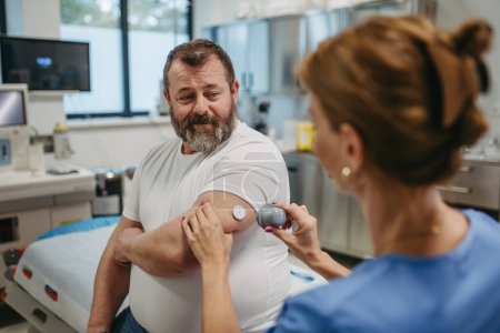 Doctor applying a continuous glucose monitor sensor on patients arm. Obese or overweight man is at risk of developing type 2 diabetes. Concept of health risks of overwight and obesity.