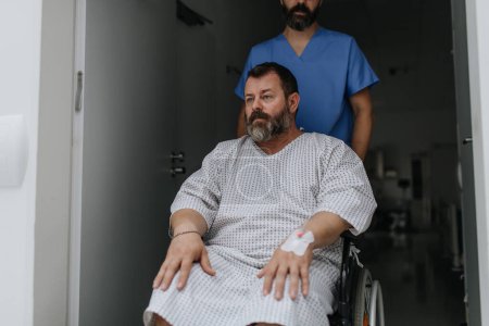 Téléchargez les photos : Une infirmière pousse un patient en fauteuil roulant le long d'un couloir de l'hôpital. Surpoids patient se sentant anxieux et a des problèmes de santé. - en image libre de droit