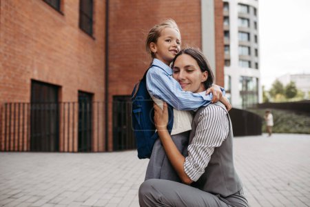 Téléchargez les photos : Une mère au travail embrassant sa fille devant le bâtiment de l'école, et se dirigeant vers le travail. Concept d'équilibre entre vie professionnelle et vie privée pour les femmes. - en image libre de droit