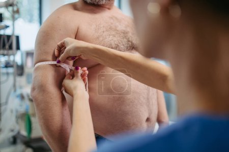 Photo for Female doctor measuring arm circumference of overweight patient using a tape measure. Obesity affecting middle-aged mens health. Concept of health risks of overwight and obesity. - Royalty Free Image