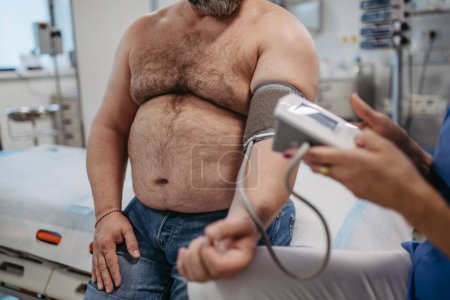 Téléchargez les photos : Médecin mesurant la pression artérielle, examinant l'hypertension, utilisant un tensiomètre. Obésité affectant la santé des hommes d'âge moyen. Concept des risques pour la santé liés à la surcharge pondérale et à l'obésité. - en image libre de droit