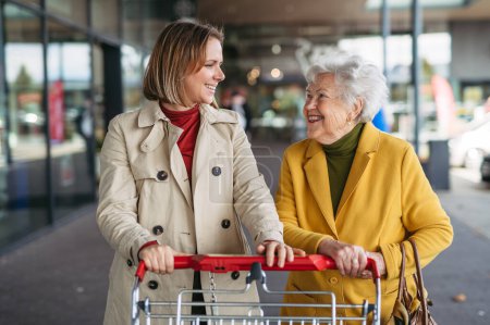 Foto de Nieta madura que lleva a su abuela de compras al centro comercial. Mujer mayor necesita ayuda con las compras de comestibles. - Imagen libre de derechos