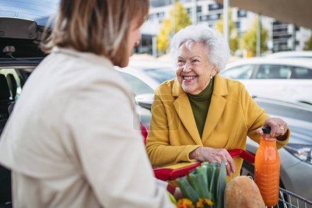 Photo for Mature granddaughter helping her grandmother load groceries in to the car. Senior woman shopping at the shopping center. - Royalty Free Image