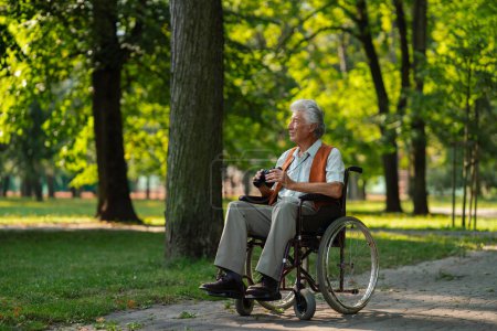 Téléchargez les photos : Homme âgé en fauteuil roulant passer son temps libre en plein air dans la nature, regarder les animaux de la forêt à travers des jumelles. - en image libre de droit