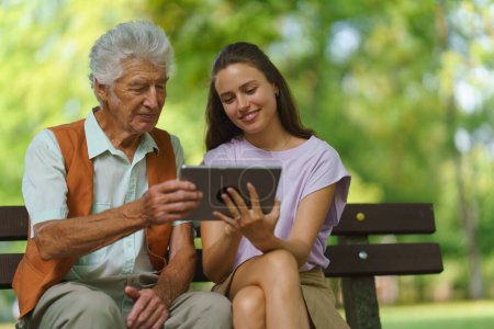 Foto de Cuidador ayudando a un hombre mayor a comprar en línea en una tableta. El riesgo de estafas de compras en línea dirigidas a las personas mayores. - Imagen libre de derechos