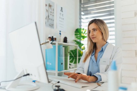Photo for Young beautiful female doctor working on laptop in doctors office. Physician doing paperwork and administrative tasks. - Royalty Free Image
