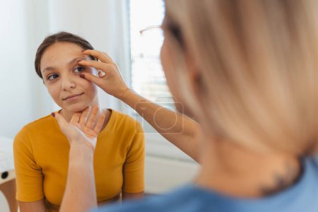 Photo for A pediatrician examining eyes of a teenage patient. Ophthalmologist treating an eye infection, allergy, or inflammation in ophthalmic clinic - Royalty Free Image