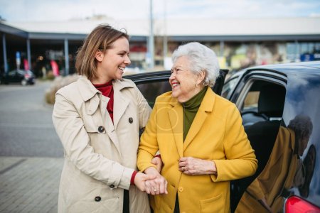 Photo for Senior lady getting out of the car, caregiver helping her, holding her hands. Elderly woman has problem with standing up from car back seat. - Royalty Free Image