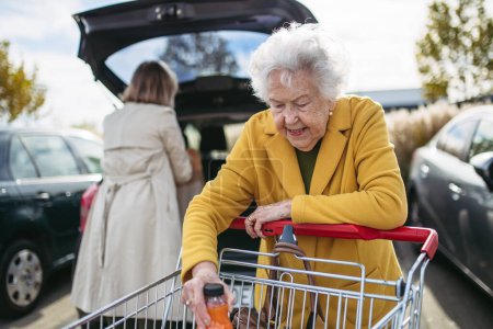 Photo for Mature granddaughter helping her grandmother load groceries in to the car. Senior woman shopping at the shopping center. - Royalty Free Image