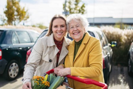 Téléchargez les photos : Petite-fille mature aidant sa grand-mère à charger les courses dans la voiture. Femme âgée faisant du shopping au centre commercial. - en image libre de droit