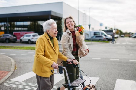 Reife Enkelin mit Omas Einkaufstasche. Seniorin und Pflegerin gehen an kalten Herbsttagen mit Ziegen aus dem Supermarkt nach Hause.