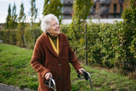 Photo for A senior woman with a mobility walker walking on the city streets during autumn day, enjoying the beautiful sunny weather. Elderly lady savoring every moment, living life to fullest. - Royalty Free Image