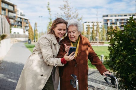 Photo for Mature granddaughter teaching grandmother how to use smartphone. Caregiver helping senior lady shopping online on her smartphone. - Royalty Free Image