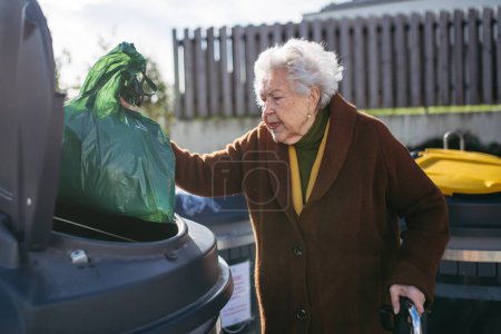Foto de Mujer mayor deshaciéndose de la basura en el cubo de basura del contenedor de residuos en frente de su complejo de apartamentos. - Imagen libre de derechos
