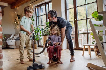 Foto de Padre e hijos limpiando la casa, aspirando pisos con una aspiradora. Niño y niña ayudando con las tareas de la casa. - Imagen libre de derechos