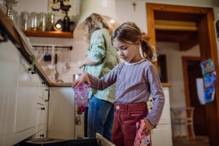 Chica tirando botellas de plástico en la papelera de reciclaje. Hija de clasificación de los residuos de acuerdo con el material en contenedores de colores en la cocina.