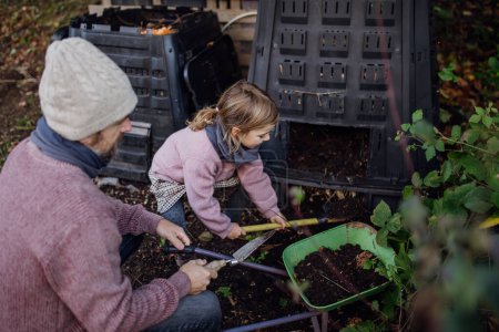 Foto de Chica ayudando a padre a eliminar el compost del compostador en el jardín. Concepto de compostaje y jardinería orgánica sostenible. - Imagen libre de derechos