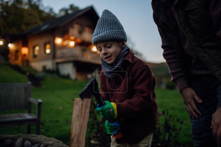 Téléchargez les photos : Jeune garçon aidant à couper un bois à l'extérieur, la préparation du bois de chauffage dans une cheminée intérieure. - en image libre de droit