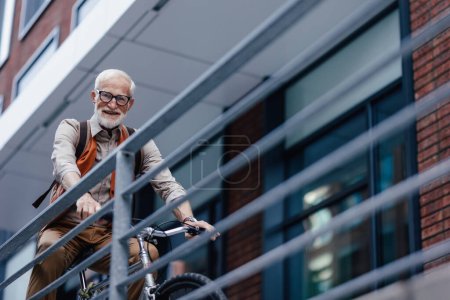Foto de Un anciano, ciclista que viaja en bicicleta por la ciudad. Viajeros mayores de la ciudad en bicicleta a la tienda de comestibles. - Imagen libre de derechos