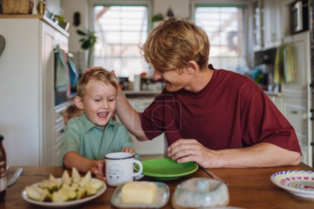 Photo for Father and son eating breakfast together in home kitchen. Healthy breakfast or fruit snack before kindergarden. - Royalty Free Image