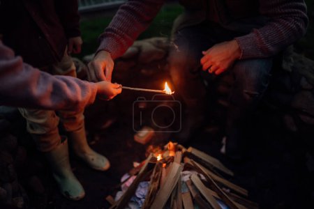 Foto de Familia pasando la noche al aire libre, encendiendo fuego en una fogata. Prents y los niños pasan tiempo familiar de calidad juntos. - Imagen libre de derechos