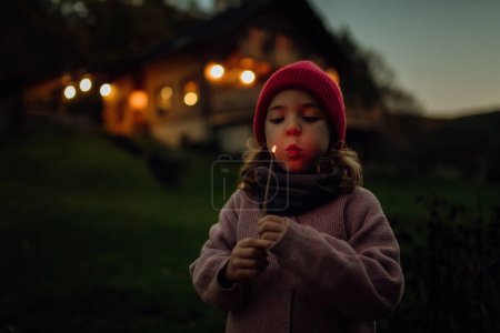 Téléchargez les photos : Portrait d'une jolie fille soufflant une flamme sur un bâton brûlant. La famille faisant un barbecue dans le jardin un soir d'automne. - en image libre de droit