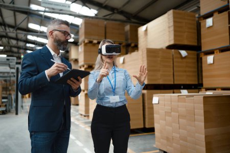 Photo for Warehouse managers talking logistics using VR, controlling stock levels, discussing shipping process. Virtual reality in inventory management. Smart glasses guiding female manager through warehouse - Royalty Free Image