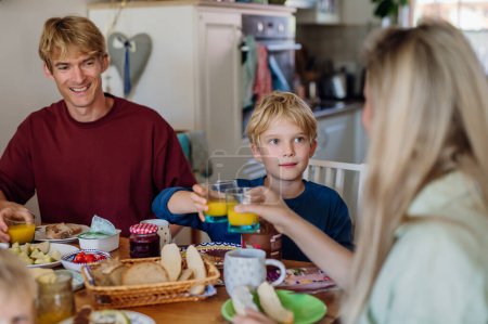 Photo for Young family eating breakfast together in home kitchen, toasting with juice. Healty breakfast or snack before school and work. - Royalty Free Image