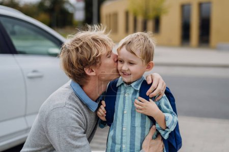 Photo for Father saying goodbyeto to son in front of school building, hugging and kissing him on the cheek. Dad heading to work. Concept of work-life balance for parents. - Royalty Free Image