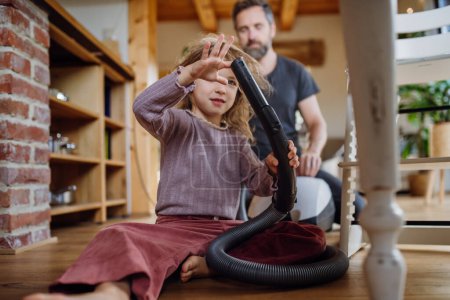 Photo for Father and daughter cleaning house, vacuuming floors with a vacuum cleaner. Young girl helping with house chores. - Royalty Free Image
