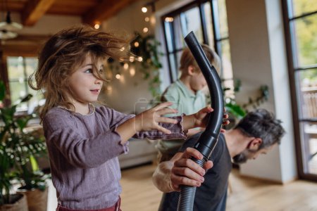 Photo for Father and son vacuuming girls hair with vacuum cleaner. Father with kids cleaning the house, helping with house chores. - Royalty Free Image